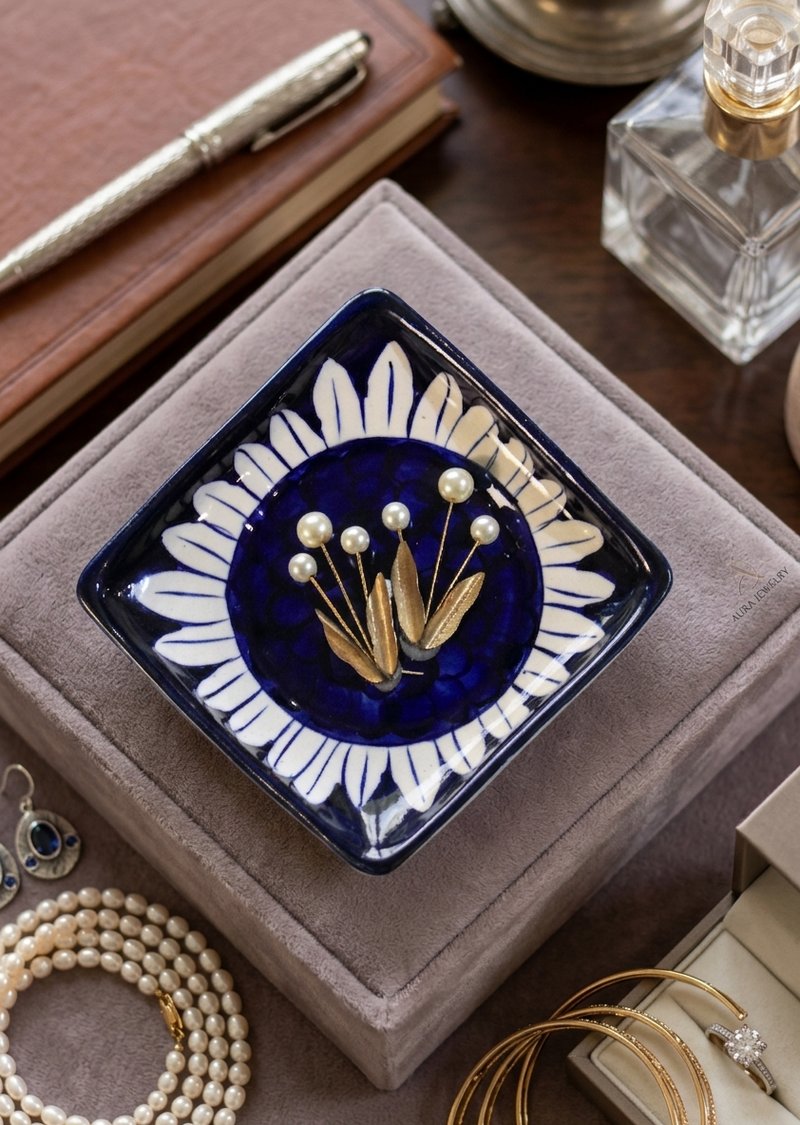 Handcrafted blue pottery square jewelry dish with a white sunflower pattern on a deep cobalt blue background and a metallic gold floral center, resting on a velvet vanity box.