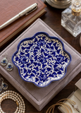 Handcrafted blue pottery scalloped jewelry dish with intricate blue and white floral pattern holding earrings on a vanity